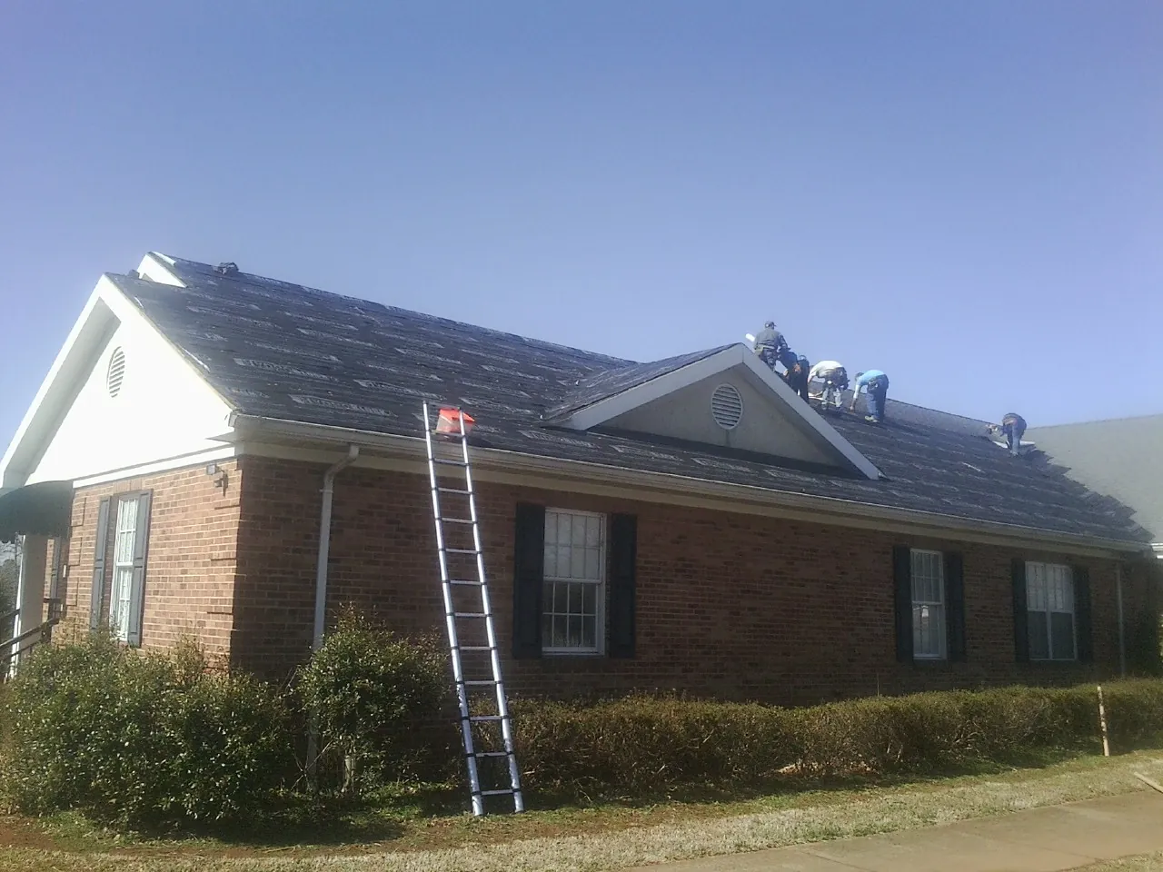 Crew tearing shingles off a brick ranch roof with a ladder set — Emergency Roof Repair work by our crew in Thurman