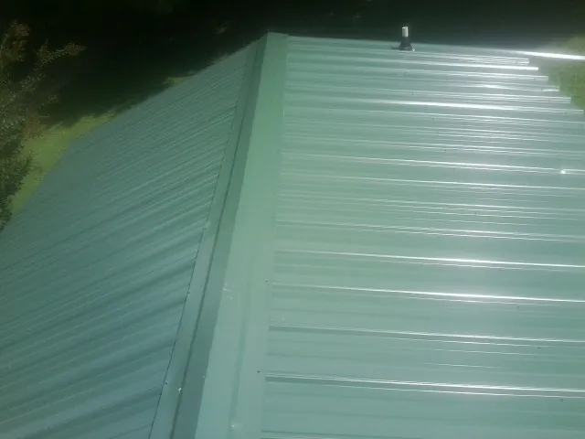 New green metal panels meeting at the ridge of a roof — Flat Roof Repair work by our crew in Thurman
