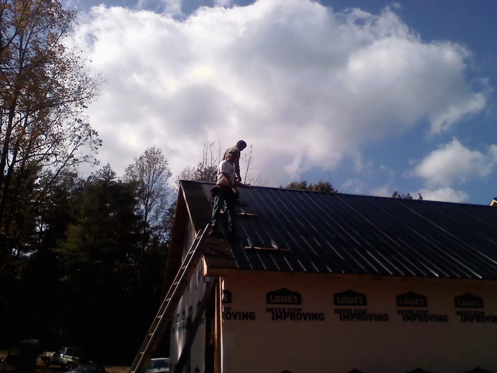 Roofer fastening dark metal panels high against a cloudy sky, from a Roof Inspection job in Thurman