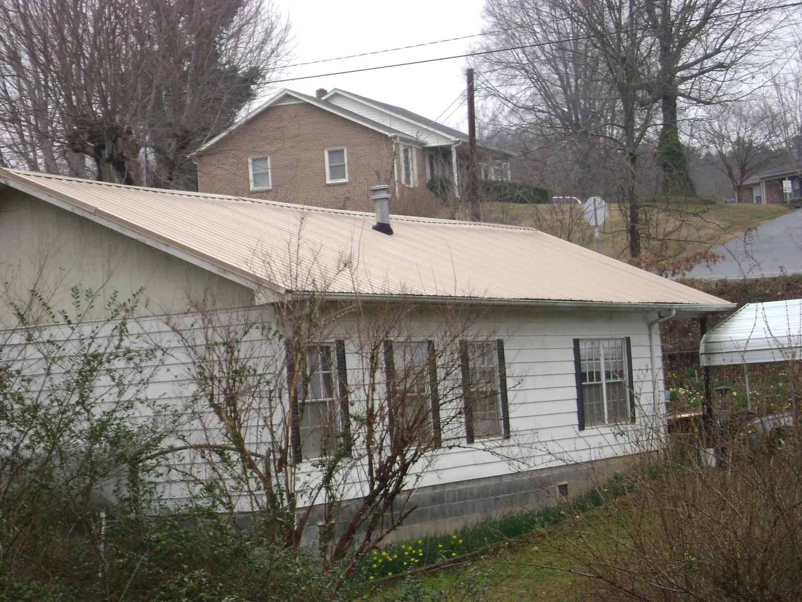 Tan metal roof on a white sided house set into a hillside — Commercial Roofing by Roofing Brothers in Thurman